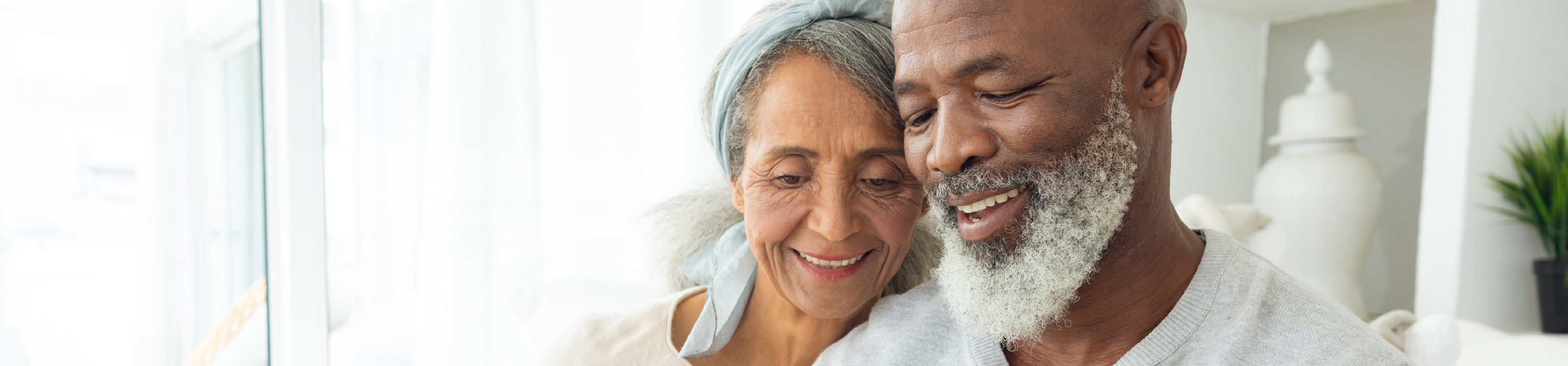 Un hombre y una mujer afroamericanos mayores sentados cerca, sonriendo y mirando hacia abajo.